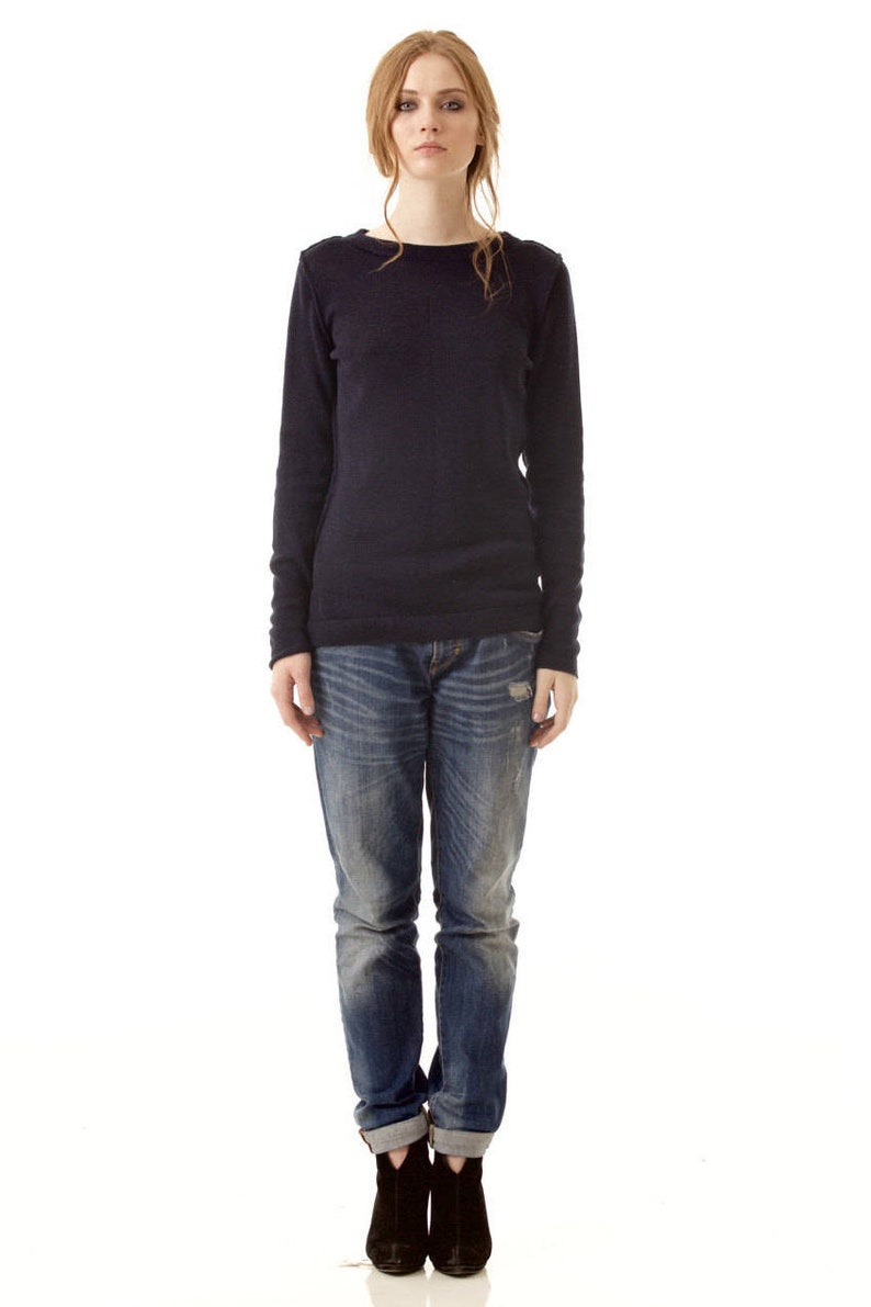May include: A long-sleeved navy blue crew neck sweater paired with blue denim jeans featuring a distressed wash and cuffed hems, worn with black ankle boots. The sweater has a simple knit texture and the jeans show faded whiskering details.