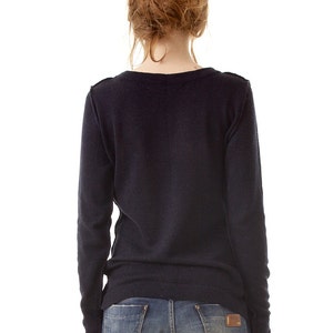 May include: A long-sleeved, dark navy blue knit sweater with a round neckline, paired with blue denim jeans featuring a brown leather patch on the back pocket. The sweater has a simple, solid-colored design with ribbed cuffs and a ribbed hemline.