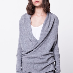 May include: A gray wrap sweater with a cowl neck and long sleeves. The sweater is made of a soft, comfortable material and has a relaxed fit.