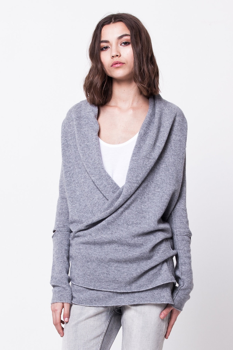 May include: A gray wrap sweater with a cowl neck and long sleeves. The sweater is made of a soft, comfortable material and has a relaxed fit.