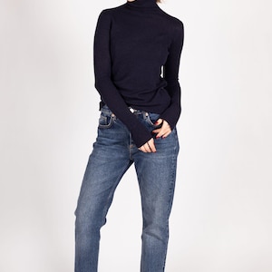 May include: A dark navy blue long-sleeve turtleneck sweater paired with medium-wash blue denim jeans and white sneakers. The sweater features a fitted silhouette with long sleeves, while the jeans have a classic straight-leg cut and a button fly.