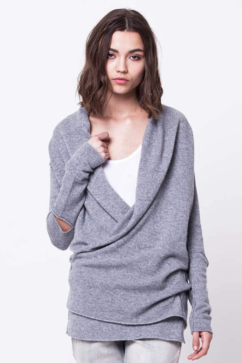 May include: A gray wrap sweater with a cowl neck and long sleeves. The sweater has a relaxed fit and a slightly longer length in the back.