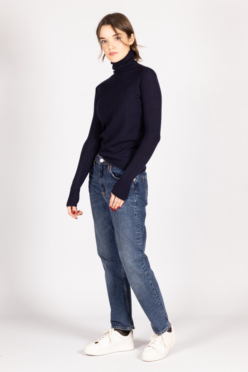 May include: A dark navy blue long-sleeve turtleneck sweater paired with medium-wash blue denim jeans and white sneakers. The sweater features a fitted silhouette with a high neck, while the jeans have a classic straight-leg cut and a button fly.