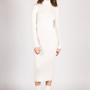 K&ouml;nnte beinhalten: Ein wei&szlig;es, geripptes Rollkragenpullover-Kleid mit langen &Auml;rmeln. Das Kleid ist figurbetont und reicht bis zur Mitte der Wade. Das Model tr&auml;gt schwarze Plateau-Heels und wei&szlig;e Socken.