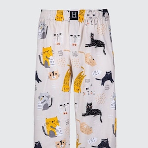 May include: Beige pajama pants with a cat print. The cats are wearing different expressions and holding milk cartons. The pants have an elastic waistband and a drawstring.