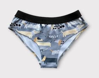 May include: Grey patterned underwear featuring dachshund dog illustrations in tan, black, and white, set against a light grey background. The underwear has a black waistband and a comfortable fit.