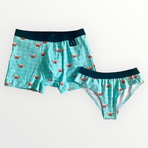 Puede incluir: Conjunto de ropa interior turquesa a juego con un estampado de cangrejos. El conjunto incluye un bóxer y una braga. Ambas piezas tienen una cinturilla azul oscuro y un patrón de cuadrícula.