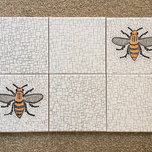 May include: Six white ceramic tiles with a mosaic pattern. Each tile features a black and orange bee with a black outline. The bees are arranged in a symmetrical pattern.