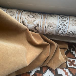 Op de afbeelding: Een bruine fluwelen stof gedrapeerd over een gepatroneerd kussen. Het kussen heeft een geometrisch ontwerp in tinten bruin, wit en beige.