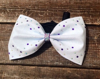 May include: White glitter bow with purple and iridescent rhinestones.
