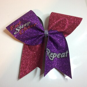 May include: Purple and red glitter cheer bow with the text "Eat Sleep Cheer Repeat" in silver glitter.