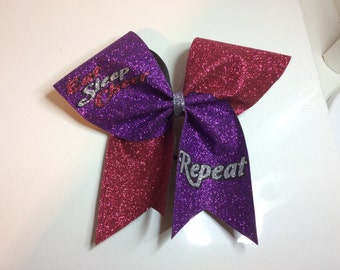 May include: Purple and red glitter cheer bow with the text "Eat Sleep Cheer Repeat" in silver glitter.