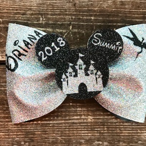 May include: A silver glitter bow with black Mickey Mouse ears. The ears have a black castle silhouette and the text "2018" on one ear and "Summer" on the other ear. The bow also has the text "Briana" on one side.