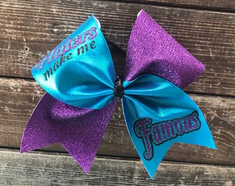 May include: A purple and blue glitter cheer bow with the text "Cheers make me famous" in black.