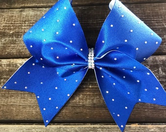 May include: A large blue cheer bow with white edges and silver glitter accents. The bow is decorated with small, clear rhinestones.