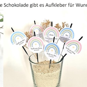 May include: Various party favors with a rainbow theme. The image shows chocolate bar wrappers, circular stickers, and sparklers, all decorated with pastel rainbows and personalized text. The text on the wrappers reads "PAUL" and "PAULA".