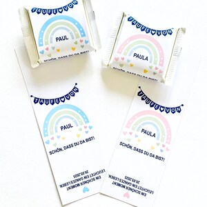 May include: White candy wrappers and bookmarks with rainbow designs. The wrappers and bookmarks feature the names "PAUL" and "PAULA", with text in German. The design includes a rainbow, hearts, and the words "TAUFE VON".