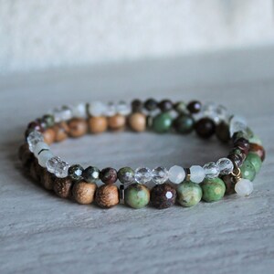 May include: A double-strand bracelet with green, brown, and clear beads. The bracelet is made of wood, gemstone, and crystal beads.