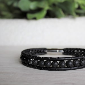 May include: A black leather bracelet with black lava rock and onyx beads. The bracelet has a silver clasp.
