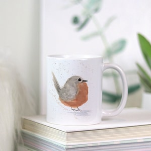 May include: White ceramic mug with a watercolor illustration of a robin bird. The bird is gray and orange with a white background.