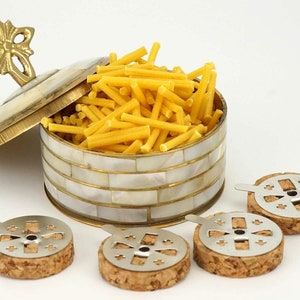 Könnte beinhalten: Ein Behälter aus Messing und Perlmutt mit Deckel und einem Schmetterlingsknopf, gefüllt mit gelben Räucherstäbchen. Vier Räucherstäbchenhalter aus Kork und Metall sind ebenfalls zu sehen.