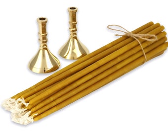 May include: A collection of long, yellow beeswax candles tied with twine, alongside two gold-colored candle holders. The candles have a natural, rustic appearance, and the candle holders have a classic, elegant design. The items are set against a white background.