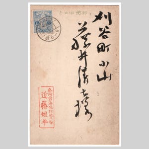 Könnte beinhalten: Eine beige Postkarte im Vintage-Stil mit vertikaler schwarzer japanischer Kalligrafie, einer blauen Briefmarke in der oberen linken Ecke mit einem runden schwarzen Poststempel und einem rechteckigen roten Stempel mit japanischen Schriftzeichen.