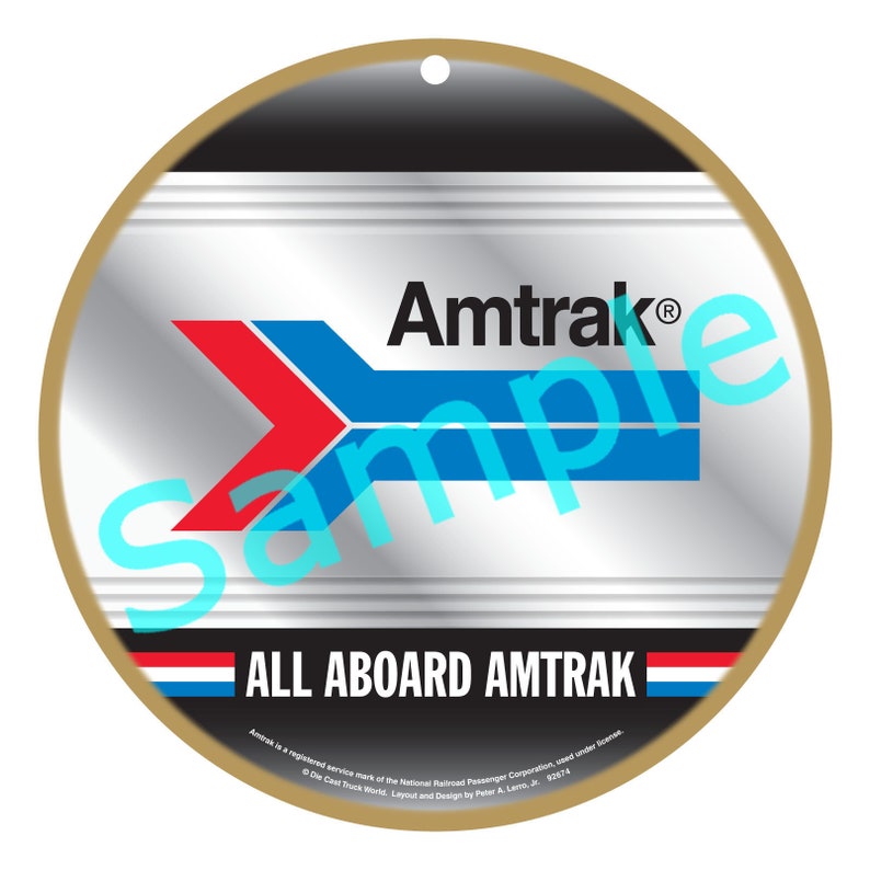 May include: A round, gold-rimmed, silver-colored ornament with the Amtrak logo and the text "ALL ABOARD AMTRAK". The Amtrak logo is a blue and red arrow pointing to the right. The text "Amtrak is a registered service mark of the National Railroad Passenger Corporation, used under license. &copy; The East Truck World. Layout and Design by Peter A. Lemo, Jr. 2017." is printed at the bottom.