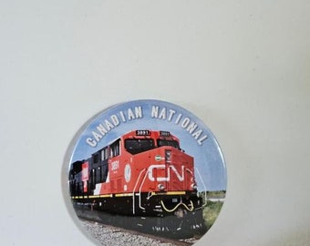 May include: A round button featuring a red, black and white Canadian National Railway locomotive against a blue background. The text "CANADIAN NATIONAL" is printed in white around the edge of the button.
