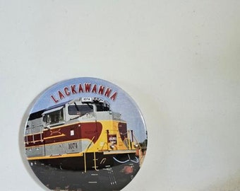 May include: A round button featuring a yellow and red train with the words "Lackawanna" and "1074" on it.