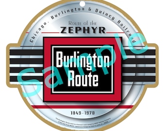 May include: A round, brown, wooden ornament with a white and silver background. The ornament features the text "Chicago, Burlington & Quincy Railroad" and "Route of the Zephyr". A red square with black text reads "Burlington Route" and "1849-1970".