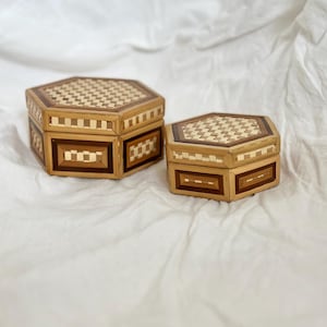 May include: Two octagonal wooden boxes with intricate geometric patterns in shades of brown and gold. The boxes are nested, with the smaller box sitting on top of the larger box.