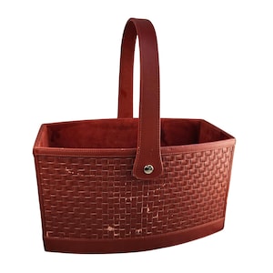 May include: A rectangular, reddish-brown basket with a woven pattern and a matching handle. The handle is attached to the basket with a silver-colored metal clasp. The interior of the basket is a solid reddish-brown color.