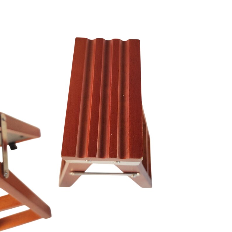 May include: Two small, reddish-brown wooden stools with a rectangular top featuring three parallel grooves. Each stool has four angled legs connected by thin metal support bars and silver-colored metal hardware at the joints and corners.
