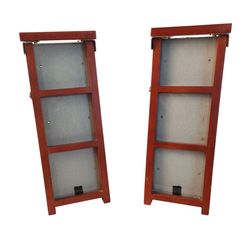 May include: Two vertical wooden picture frames with a reddish-brown finish. Each frame features three rectangular openings arranged in a column, with light gray backing boards visible through the openings and metal hinges at the top edges.