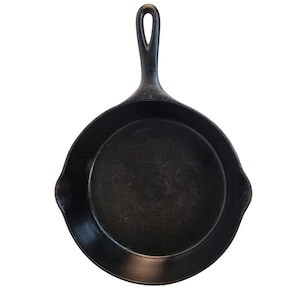 May include: A black cast iron skillet with a long handle and a loop for hanging. The skillet has a round cooking surface and two small spouts on either side. The pan is made of heavy-duty metal and is designed for cooking.