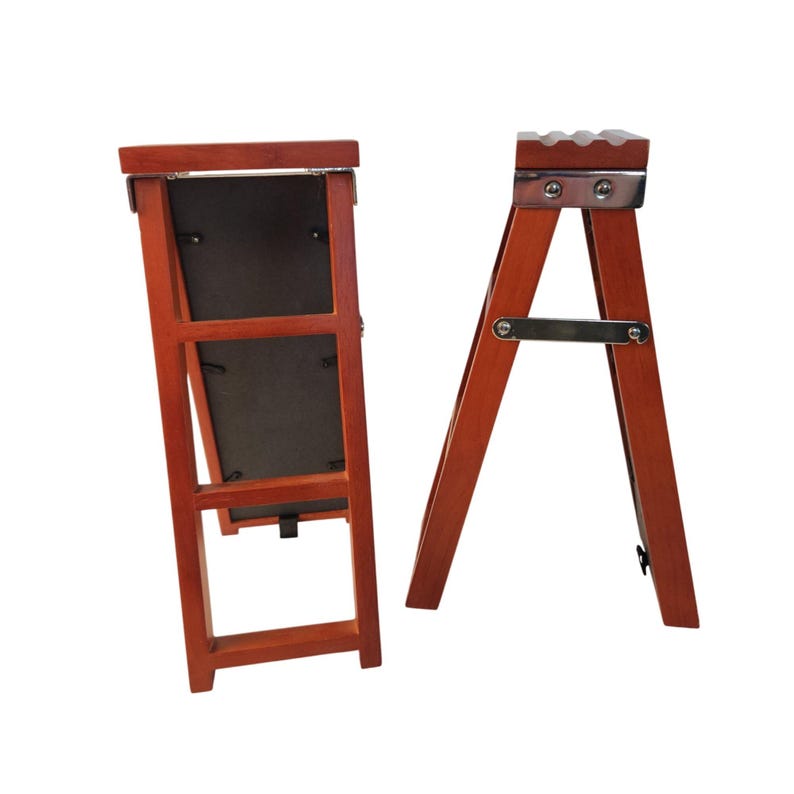 May include: Two wooden easel-style stands with a reddish-brown finish. The left stand features a rectangular frame with a dark backing, while the right stand has a metallic top bracket and a horizontal metal support bar connecting the legs.