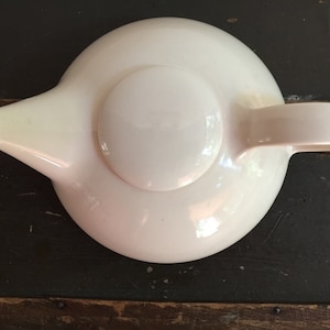 May include: A white ceramic teapot with a round body and a lid. The teapot has a spout and a handle.