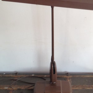 May include: A brown metal desk lamp with a long, adjustable arm and a rectangular base. The lamp has two switches on the top of the arm.