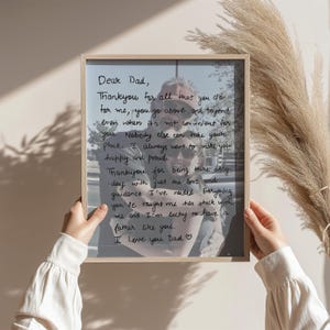May include: A framed print with a handwritten message to "Dear Dad" in black ink. The message is overlaid on a black and white photograph. The frame is a light wood color.