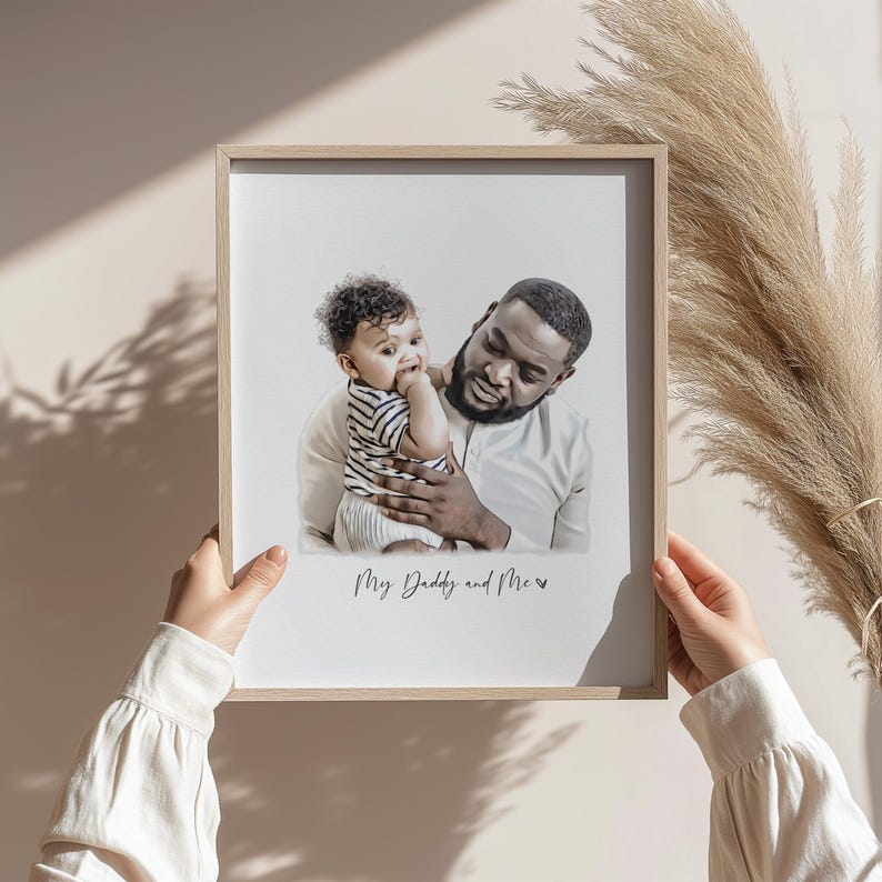 Może przedstawiać: Oprawiony wydruk przedstawiający ojca i dziecko. Dziecko, w koszuli w paski, jest trzymane przez ojca. Na wydruku widnieje napis "My Daddy and Me". Rama jest z jasnego drewna.