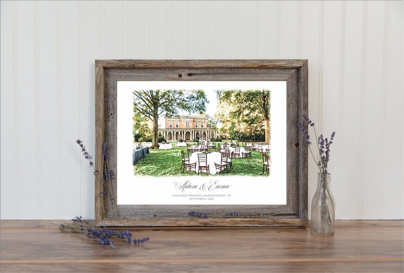 May include: A framed print featuring a wedding scene with a historic building in the background. The print is in a rustic wooden frame. The image includes tables and chairs set up on a lawn, with text that reads "Adam & Emma".