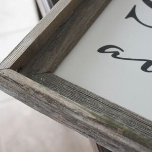 May include: Close-up of the corner of a rustic wood frame with a white background. The frame is made of weathered wood with a gray and brown color.