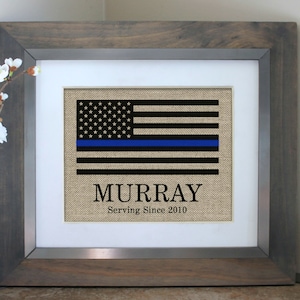 May include: Framed burlap print of an American flag with a blue line, the name "MURRAY" and the text "Serving Since 2010".