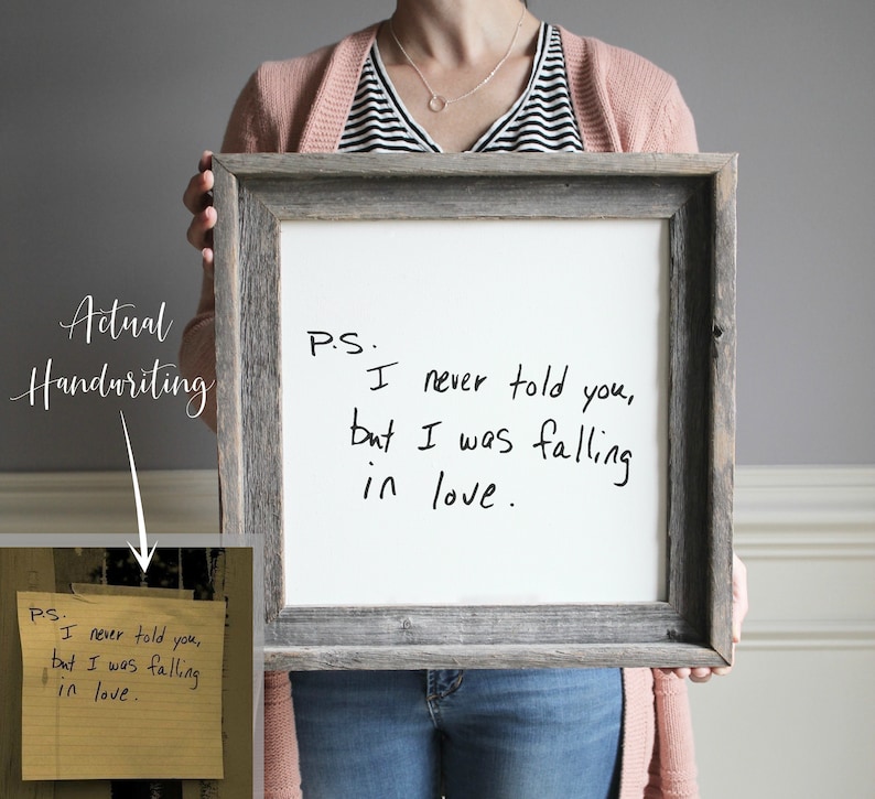May include: A framed white board with the handwritten message "PS. I never told you, but I was falling in love." The board is held by a person wearing a pink striped sweater and blue jeans.