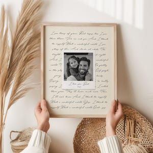 May include: A framed print featuring the lyrics to What a Wonderful World in black cursive script on a beige background, with a central square black and white photograph of a man and a child, including the handwritten text I love you Dad, Katie.