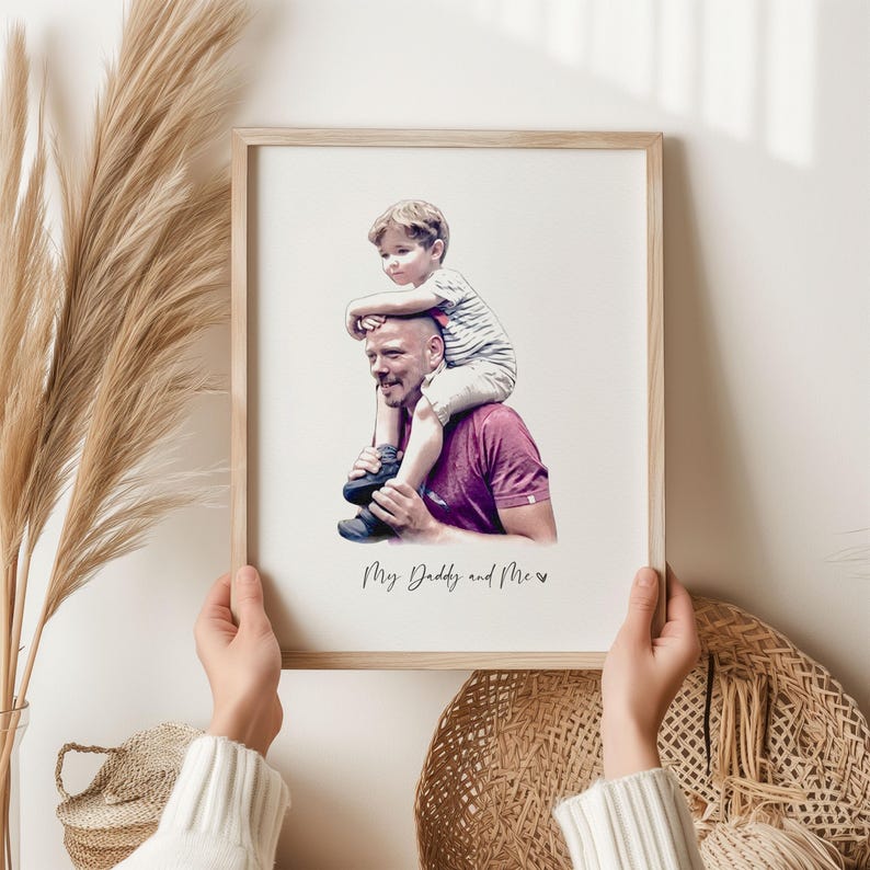 May include: A watercolor-style illustration of a father and son. The son is sitting on the father's shoulders. The image is framed in a light wood frame and has the text "My Daddy and Me" written below the image.