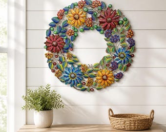 May include: A circular metal wall art piece featuring a vibrant floral wreath design. The sculpture displays multi-colored flowers in shades of yellow, red, and blue, interspersed with green leaves and small berry-like accents throughout the frame.