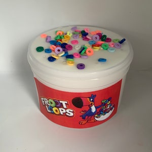 May include: A white plastic container filled with white slime and topped with colorful cereal-shaped sprinkles. The container has a red label with the words "Froot Loops" and a cartoon toucan holding a bowl of cereal.