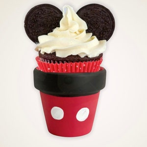 May include: A whimsical cupcake creation resembling a famous cartoon character. The cupcake features a chocolate base with white frosting, set in a red pot with white polka dots. Oreo cookies form the ears, creating a playful design.
